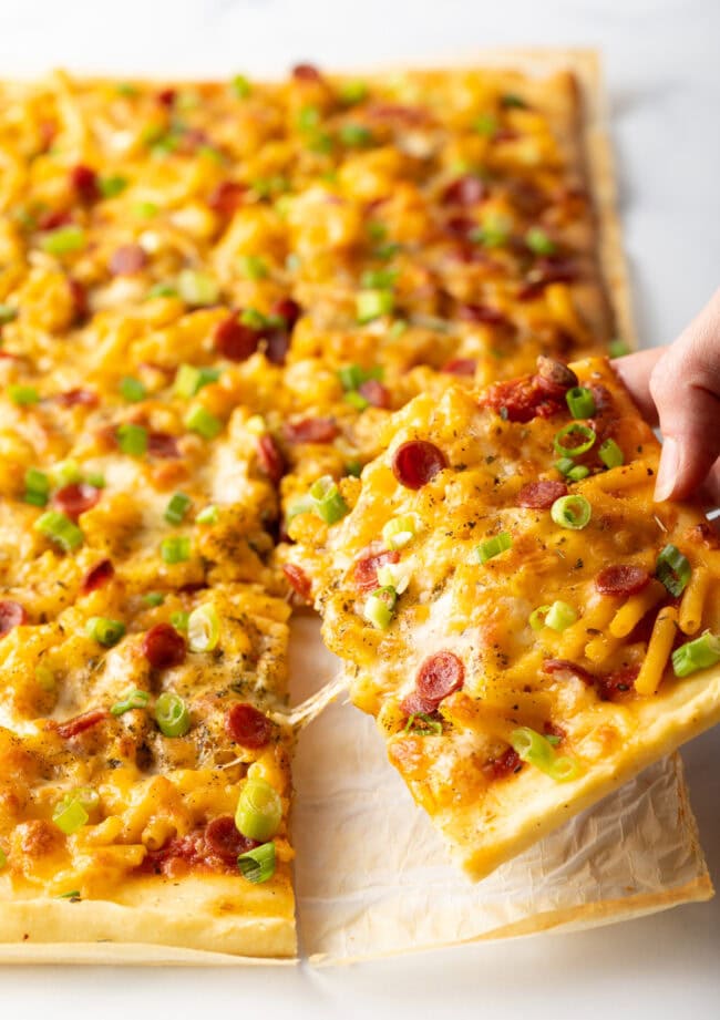 Hand pulling off a piece of mac and cheese pizza. 