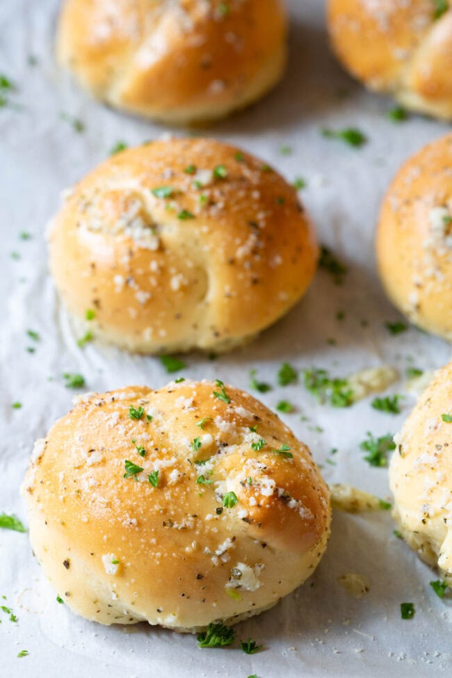Garlic knots lined up on a baking sheet lined with parchment paper.