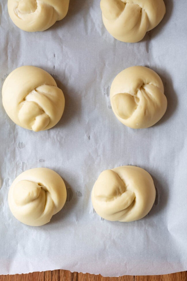 Uncooked garlic knots on a parchment lined baking sheet.
